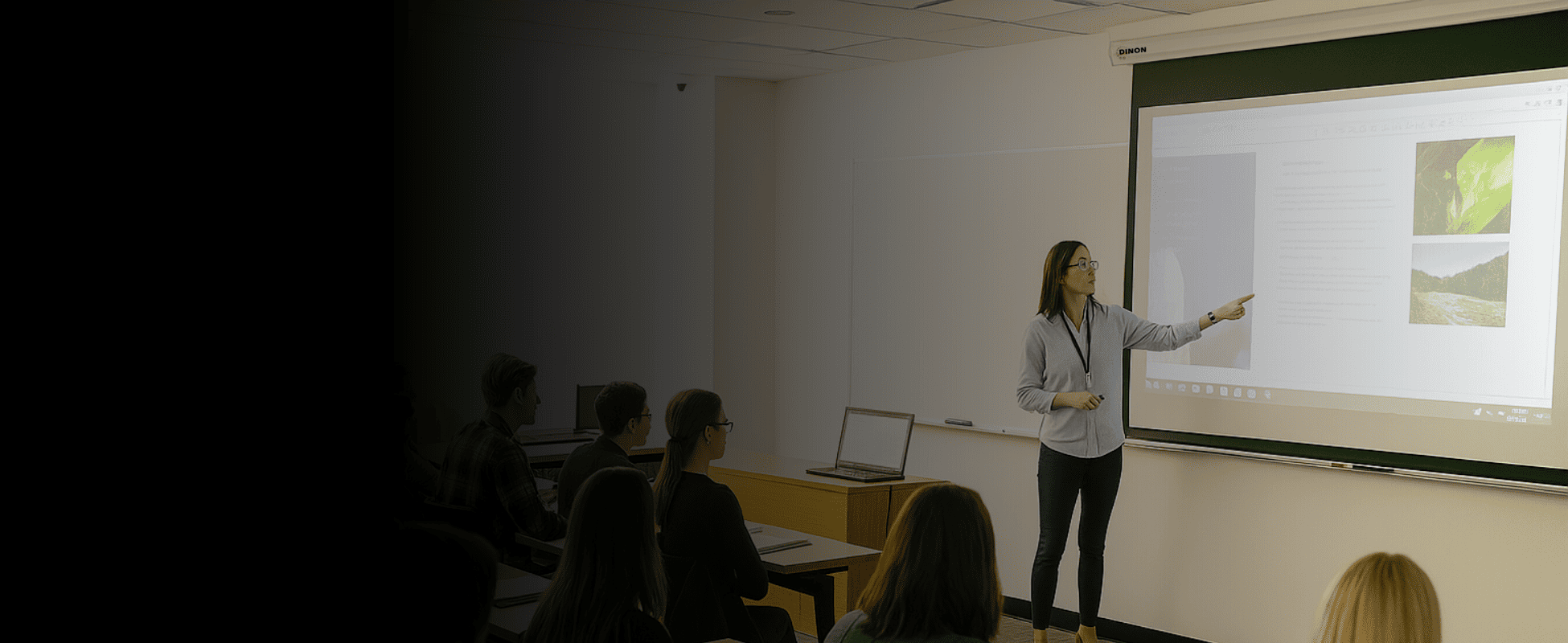 telon-dinon-aula-clases-profesora Profesora dando clases y señalando un telón Dinon en el salón de clases